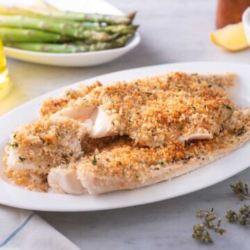 baked haddock on white plate with asparagus in background