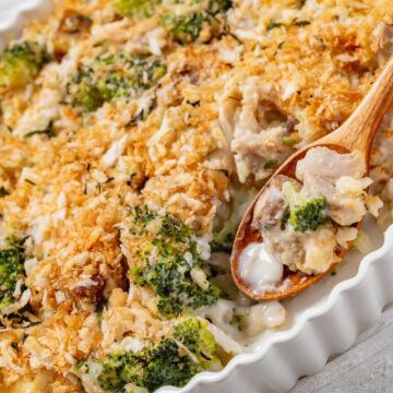 chicken broccoli casserole in white baking dish with wooden spoon