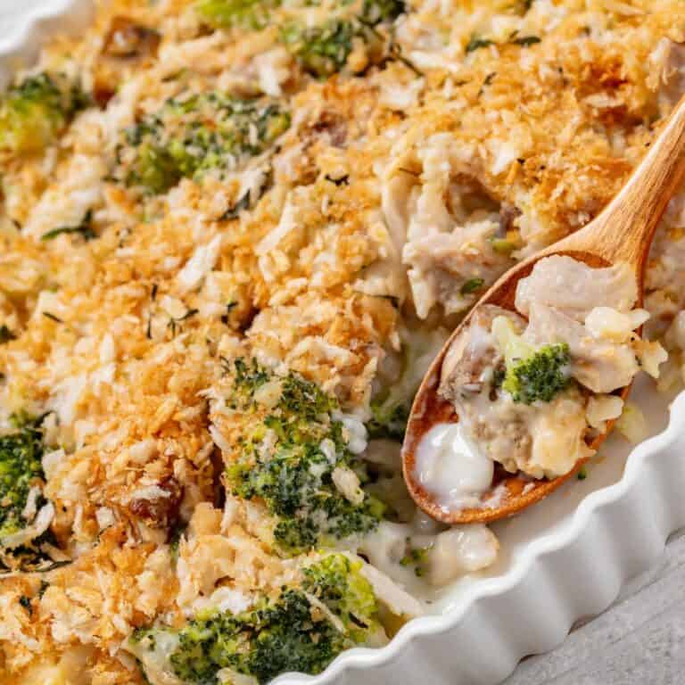 chicken broccoli casserole in white baking dish with wooden spoon