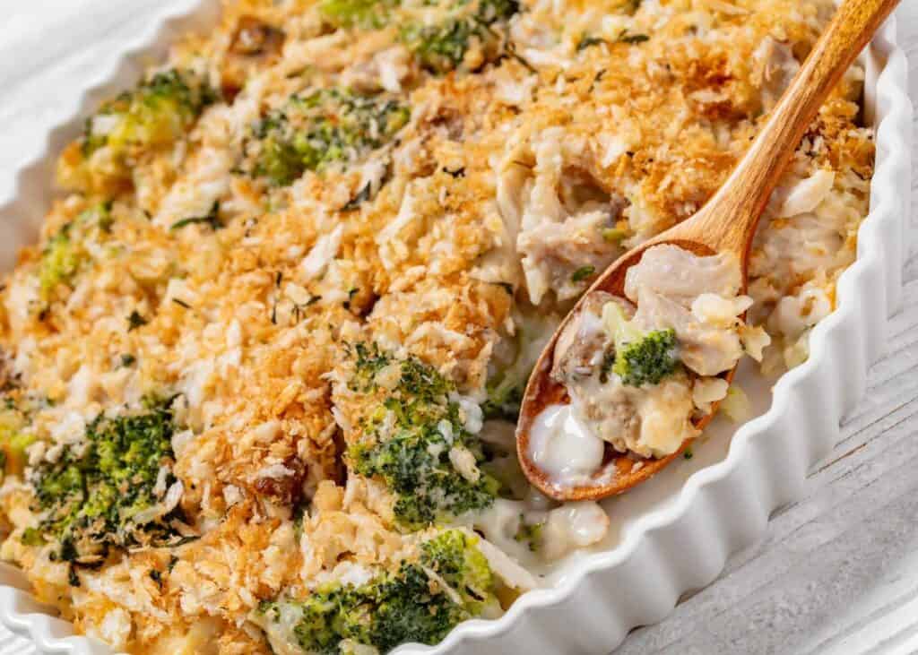 chicken broccoli casserole in white baking dish with wooden spoon