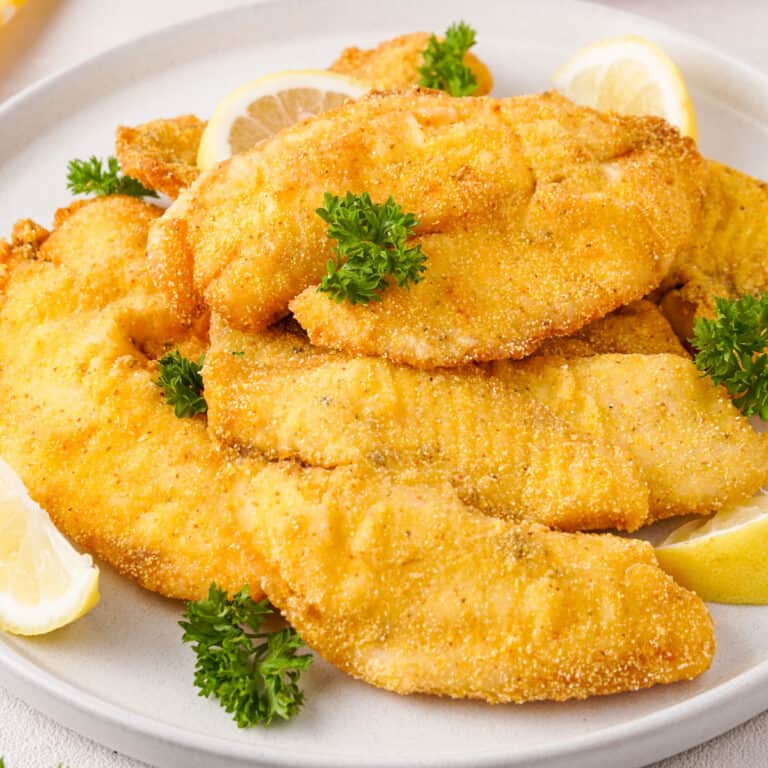 fried fish filets on white plate with lemon wedges