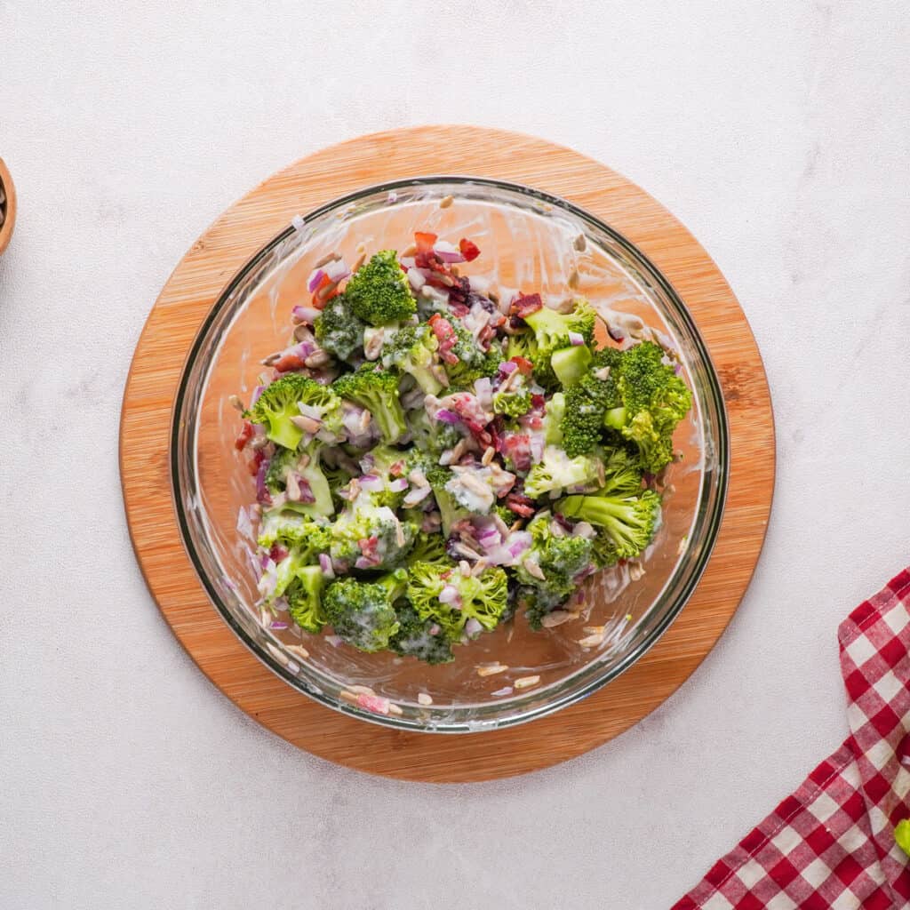 mixing broccoli salad and dressing in glass bowl