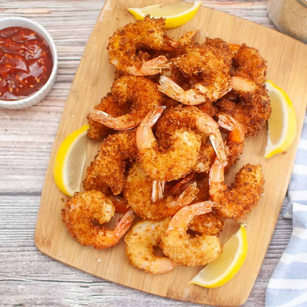 panko fried shrimp on cutting board with lemon wedges and cocktail sauce