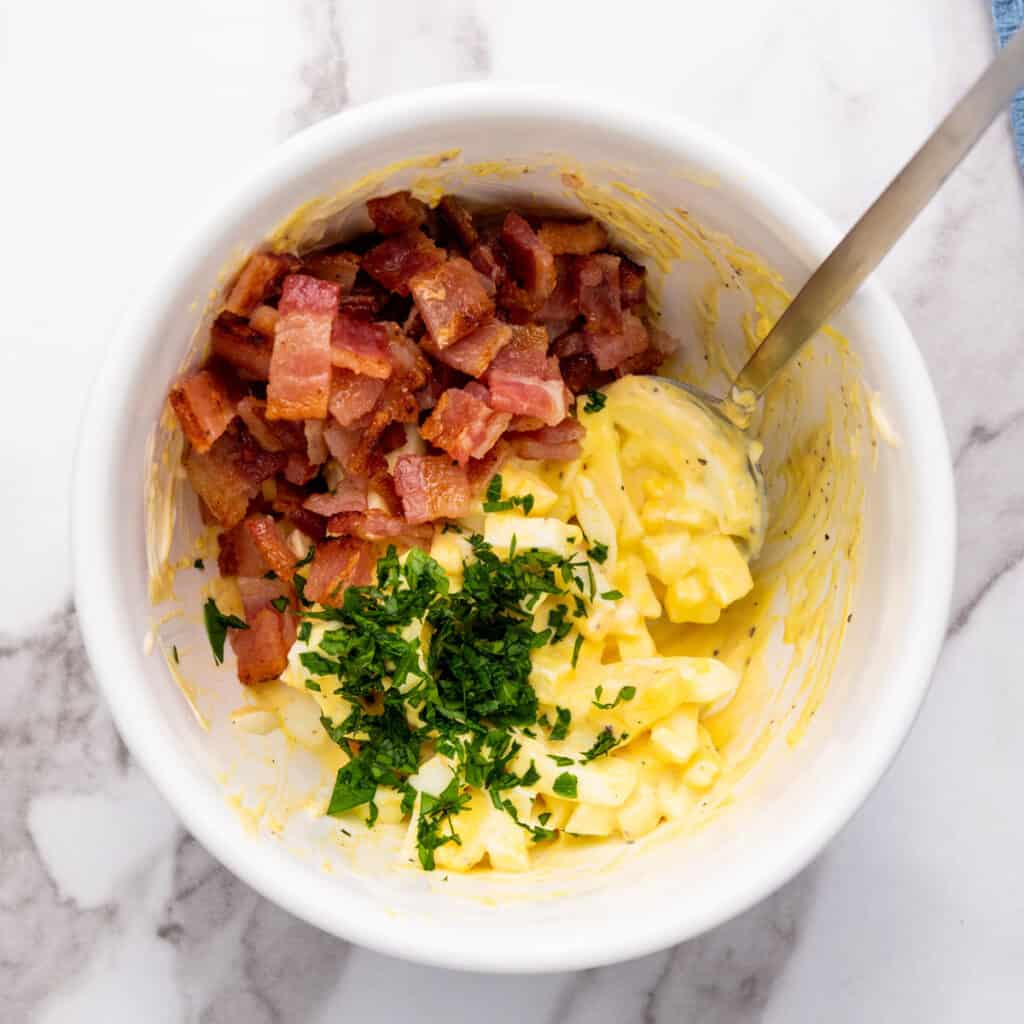 mixing egg salad with bacon in a bowl