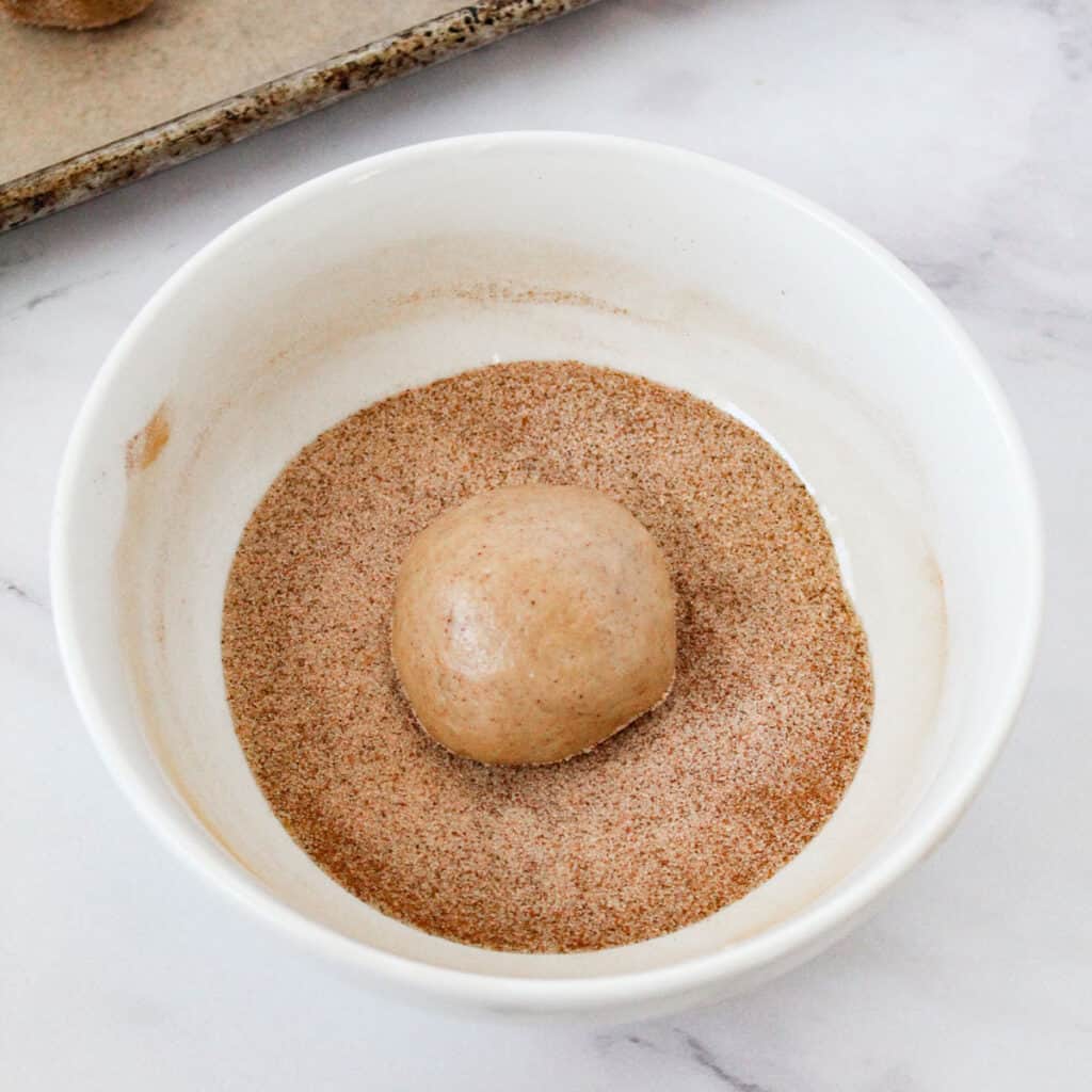 rolling chewy snickerdoodle dough ball in cinnamon sugar