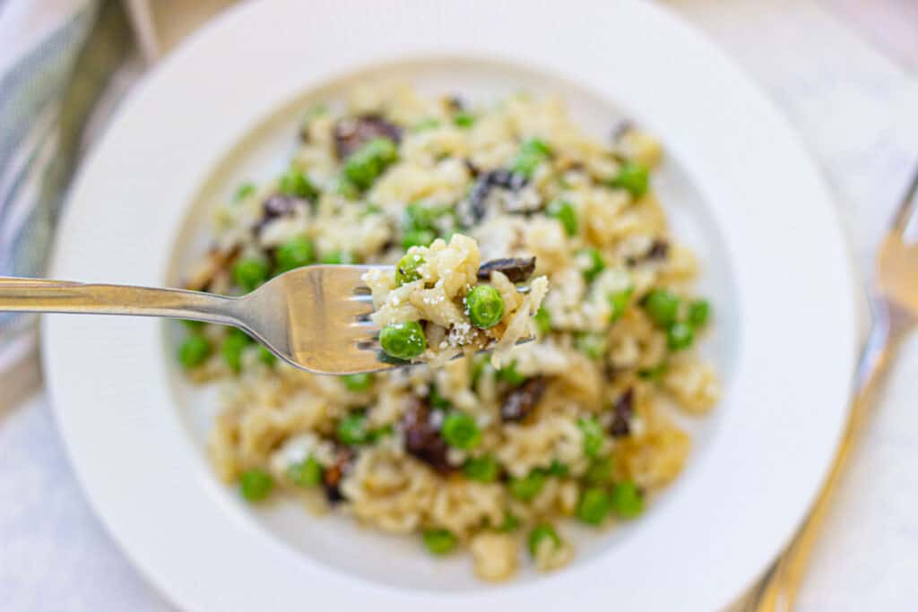 fork holding bite of risotto with peas over bowl