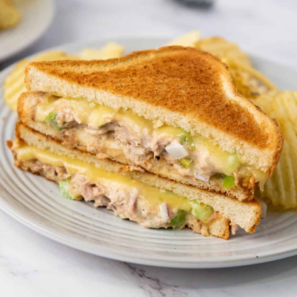 two halves of a tuna melt stacked on a plate with chips