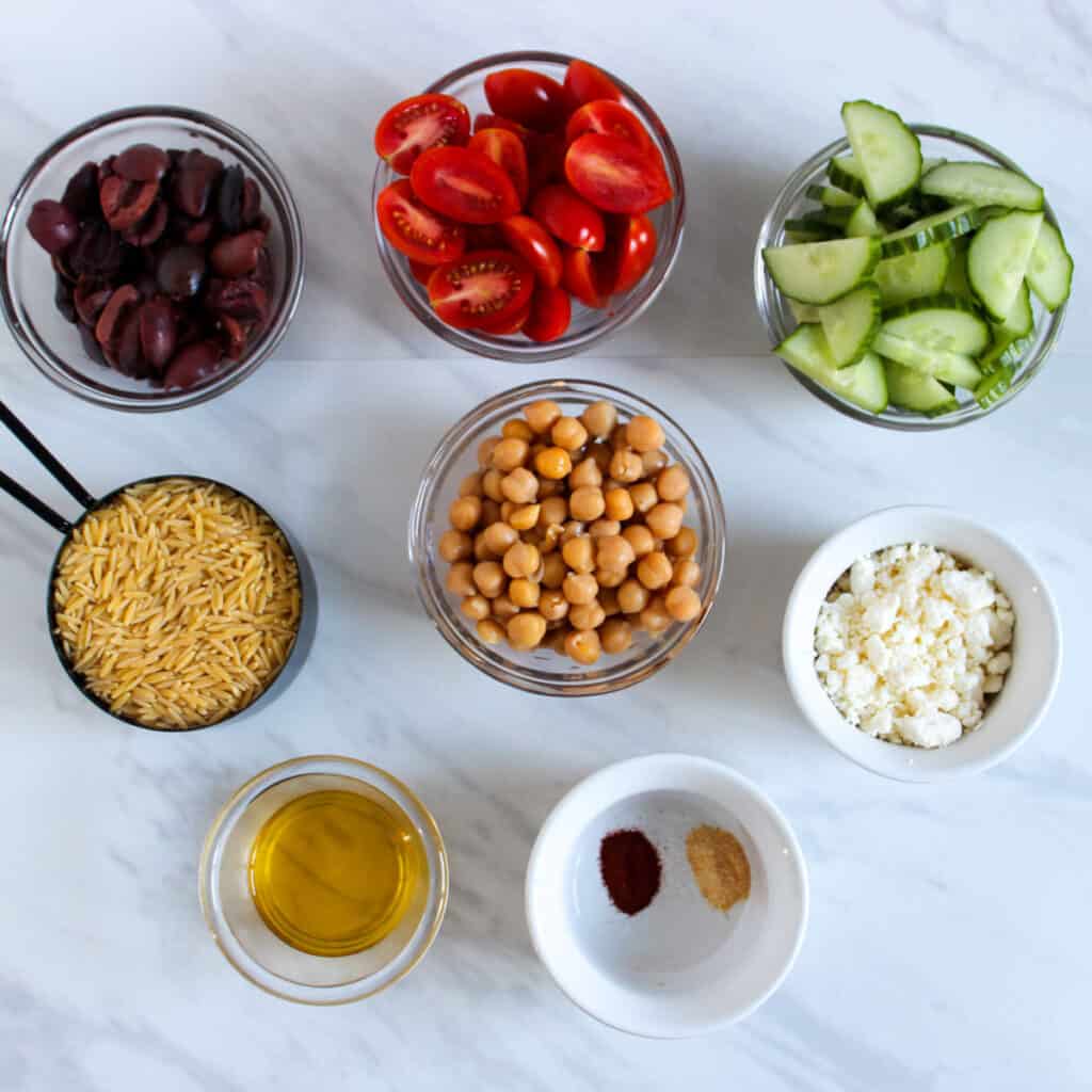 Greek orzo salad ingredients in bowls on countertop