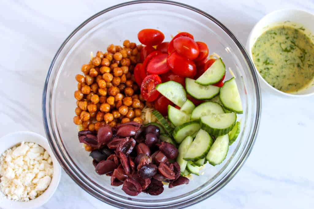 Greek orzo salad before mixing in glass bowl