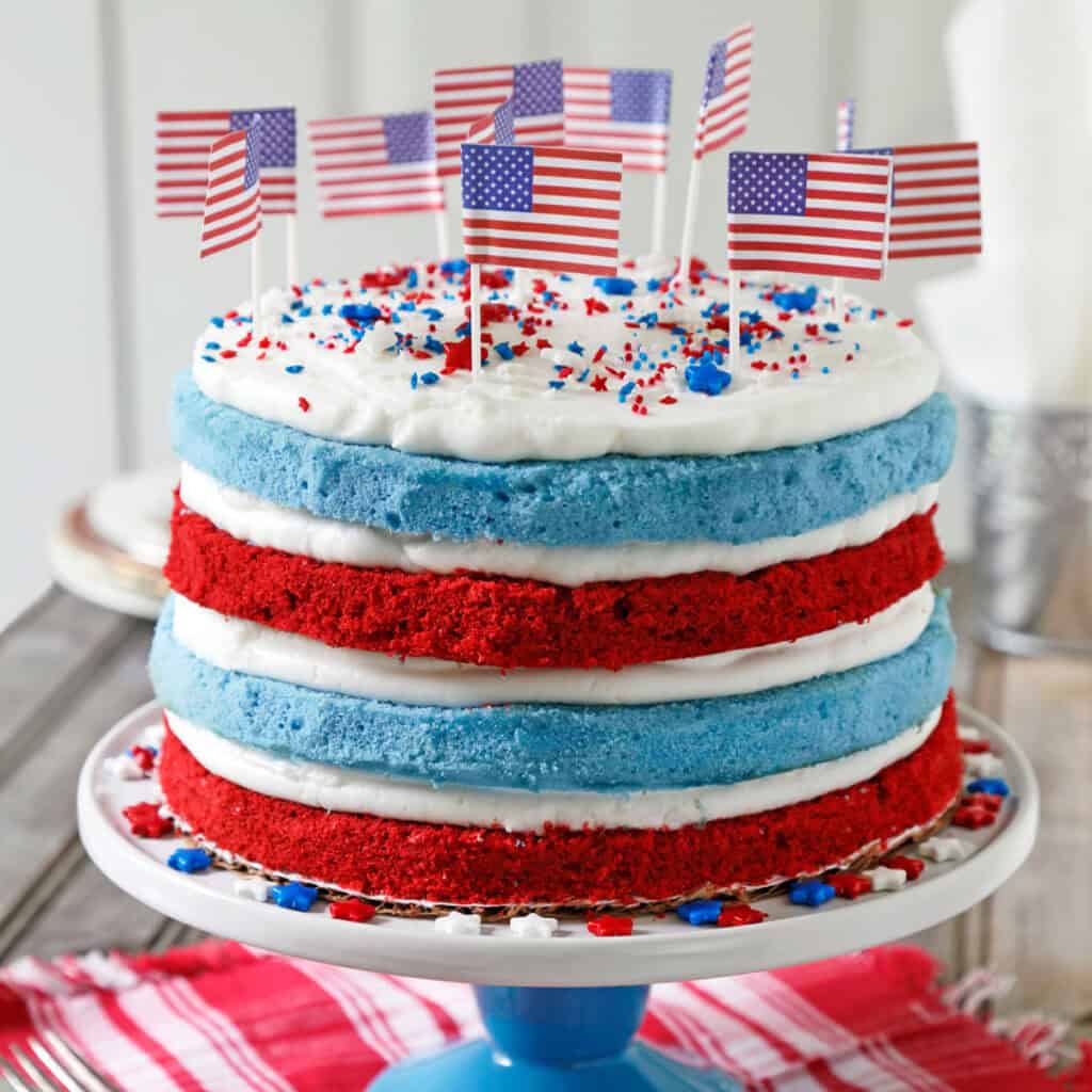 red, white, and blue layered cake with USA flags and sprinkles on top