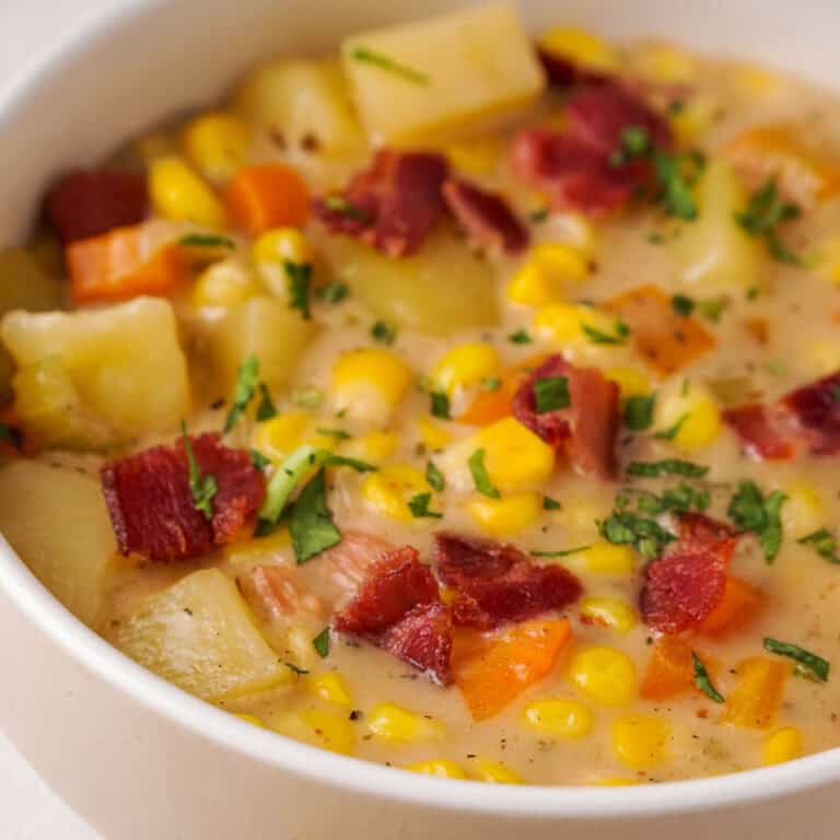 close up of corn chowder with bacon and potatoes in white bowl