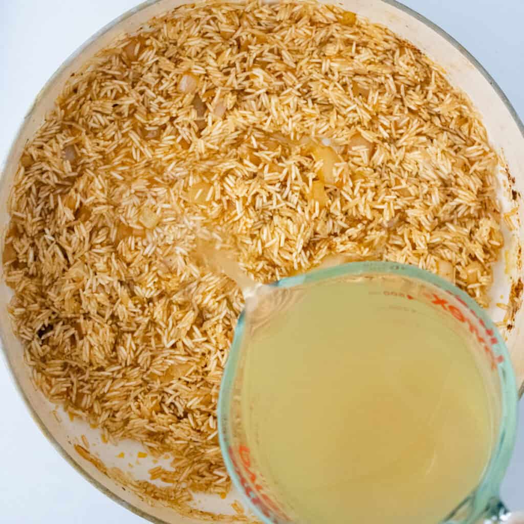 pouring broth into skillet of rice