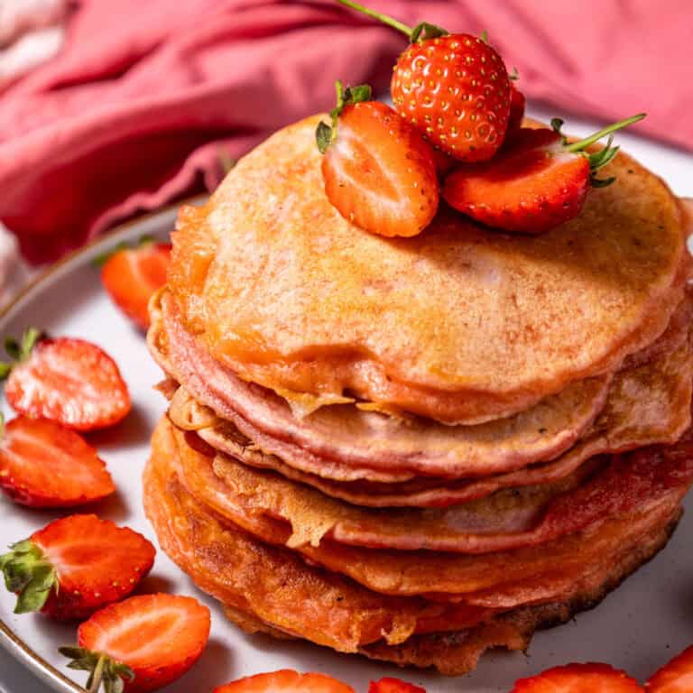 strawberry pancakes stacked on plate with sliced strawberries
