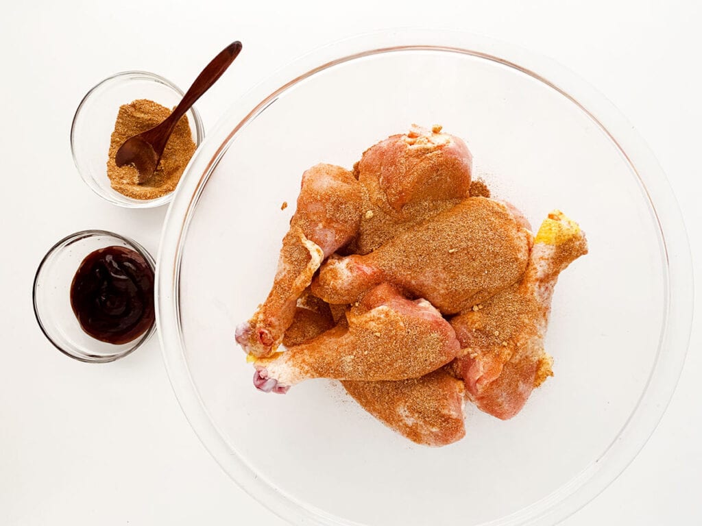 coating slow cooker barbecue drumsticks with seasoning in glass bowl