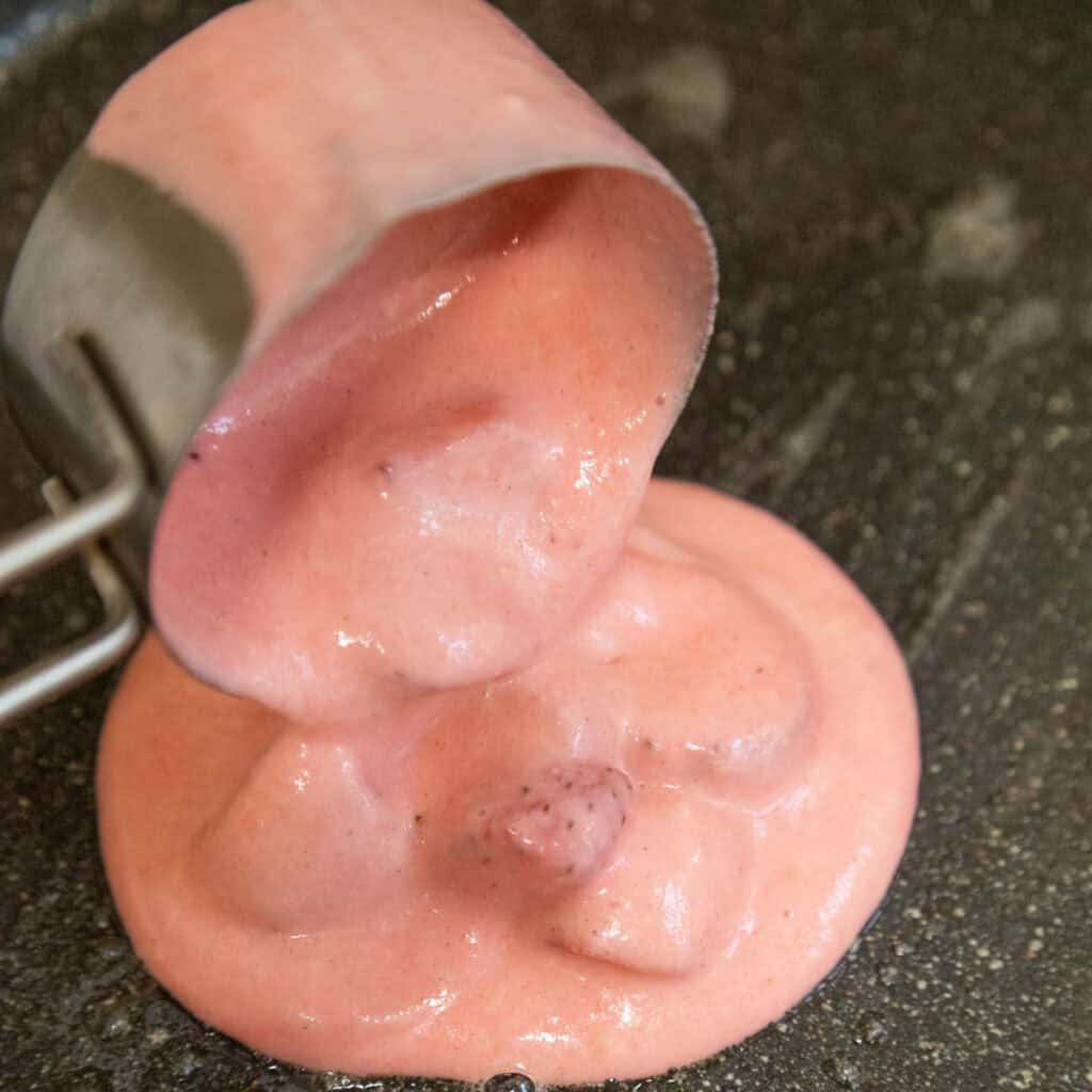 pouring strawberry pancakes batter on griddle