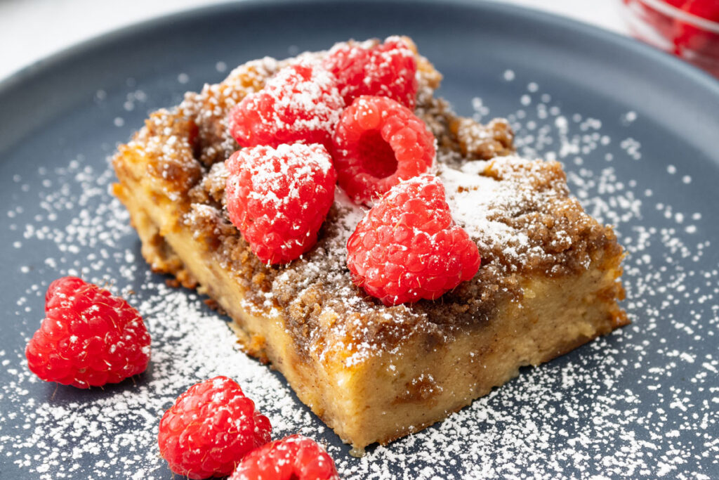 piece of French toast casserole with raspberries and powdered sugar on grey plate