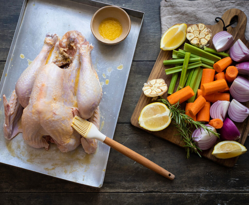 brushing melted butter on turkey next to chopped vegetables
