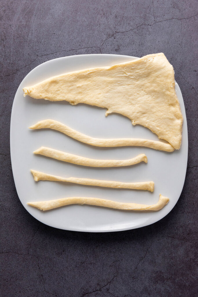 cutting crescent roll dough into strips on white plate