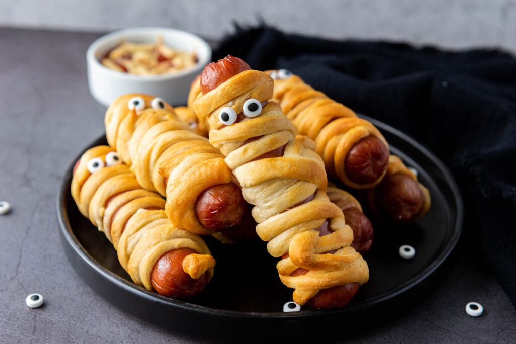 mummy hot dogs on black plate with dipping sauce