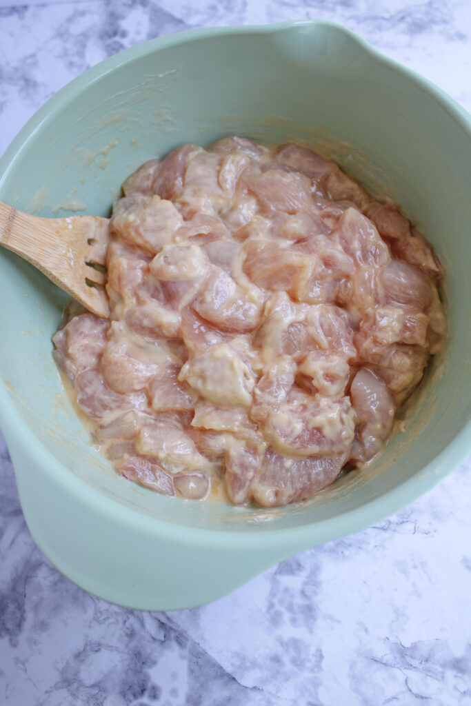 stirring raw chicken pieces with egg and flour coating