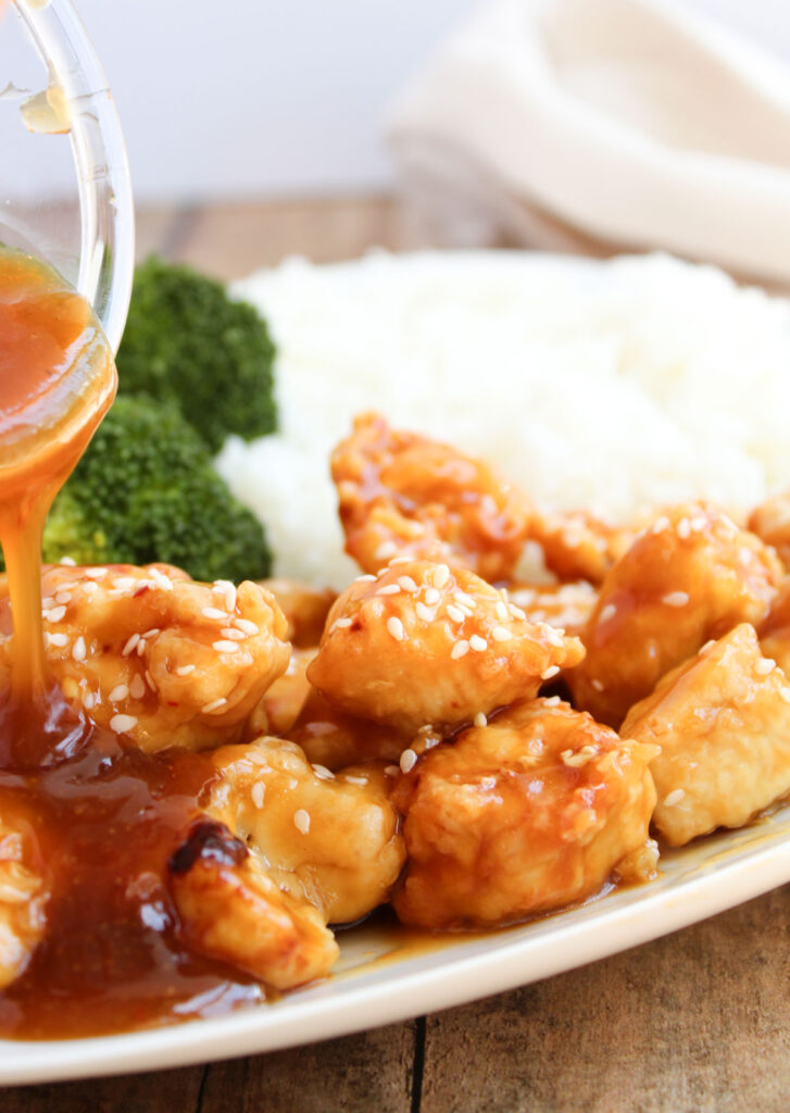 pouring sauce over orange chicken