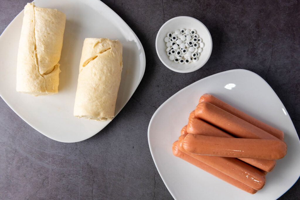 hot dogs, crescent rolls dough, and eyeball candies on white plates
