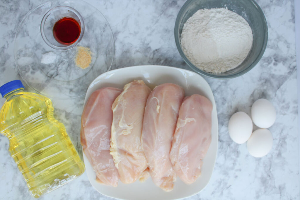 chicken cutlets and spices and flour in bowls on counter