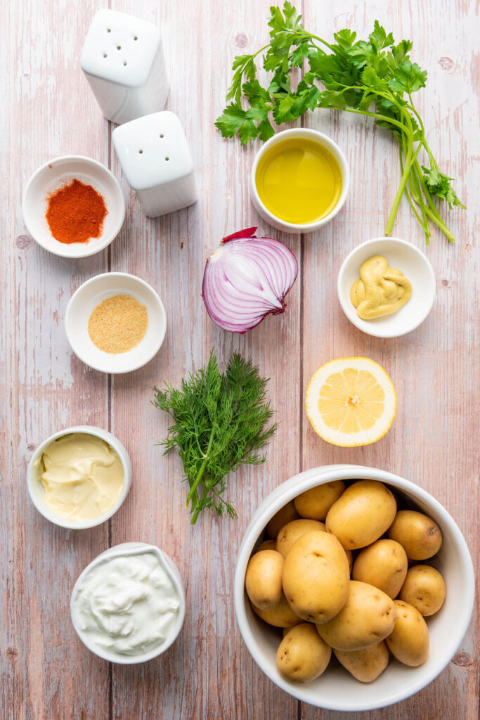smashed potato salad ingredients in white bowls on wood table