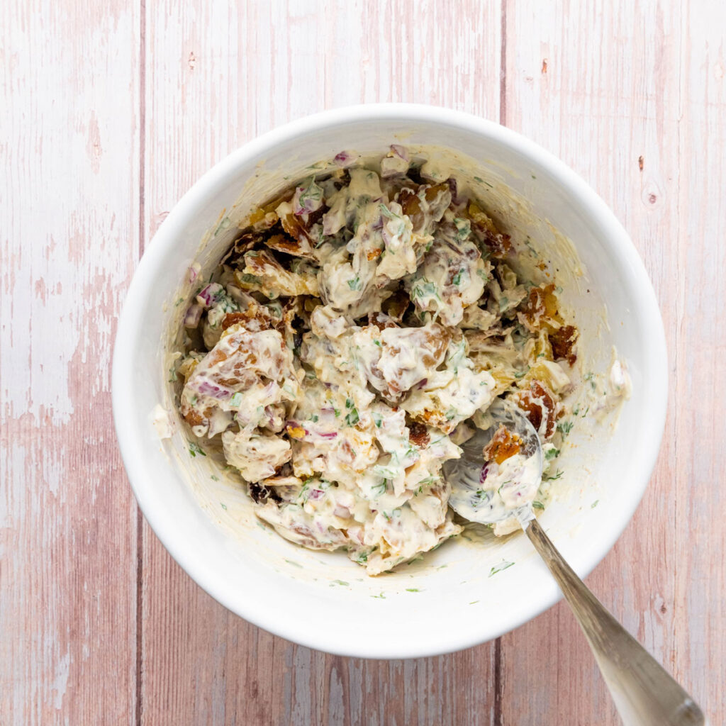 stirring smashed potato salad in a white bowl