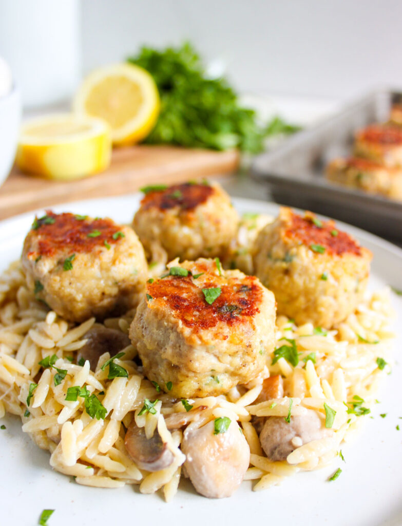 white plate with orzo topped with chicken meatballs