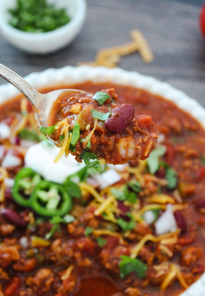 spoon full of crock pot chili held over bowl