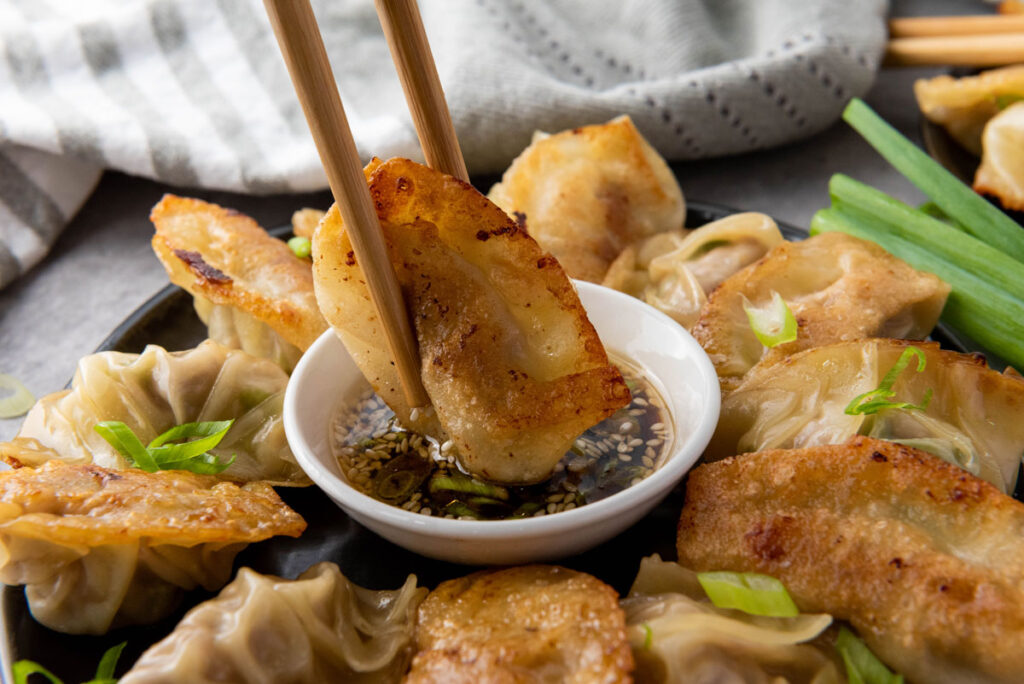 chopsticks dipping pan fried pork dumpling in sauce