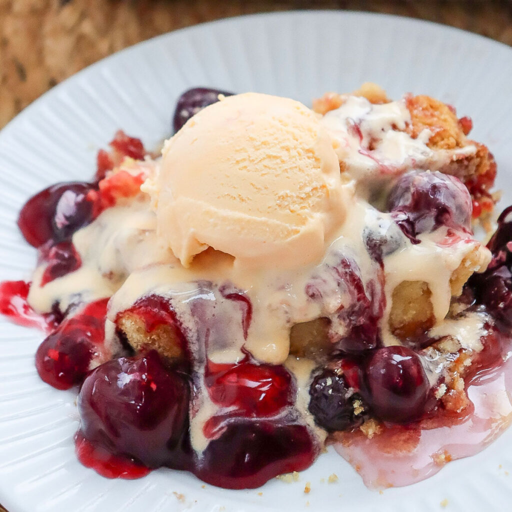 cherry dump cake with scoop of vanilla ice cream on white plate