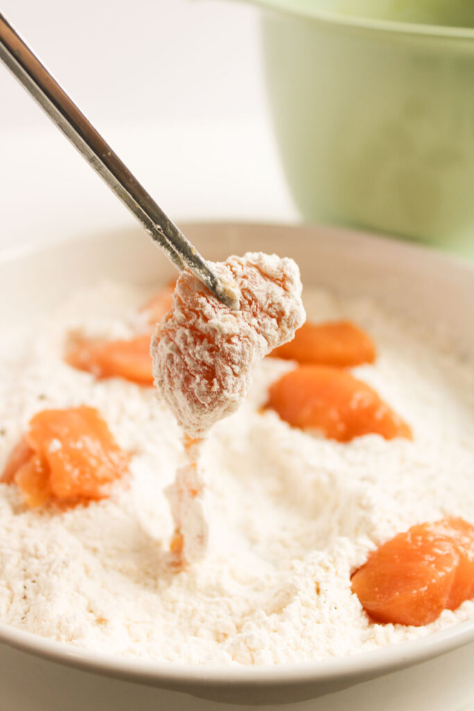 chopsticks holding chicken piece in breading
