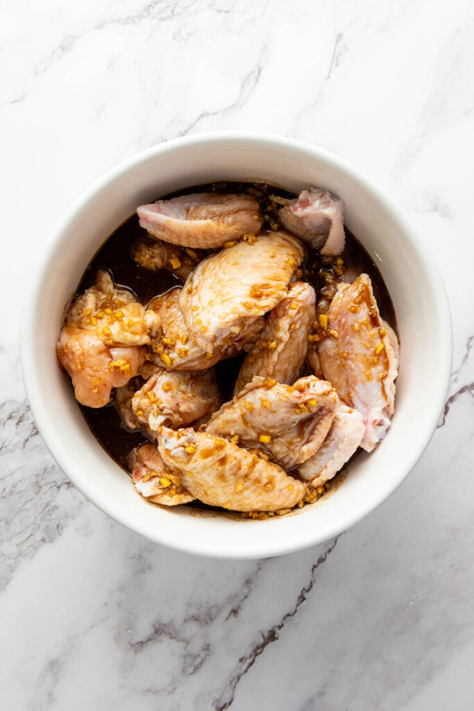 asian sticky wings marinating in sauce in white bowl