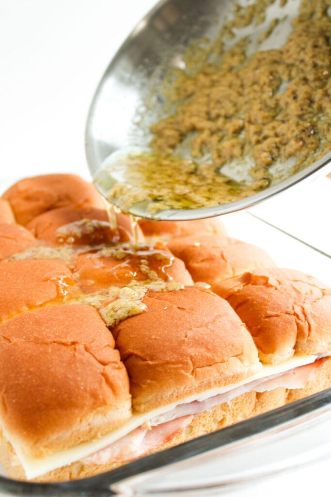 pouring butter sauce over ham and swiss sliders