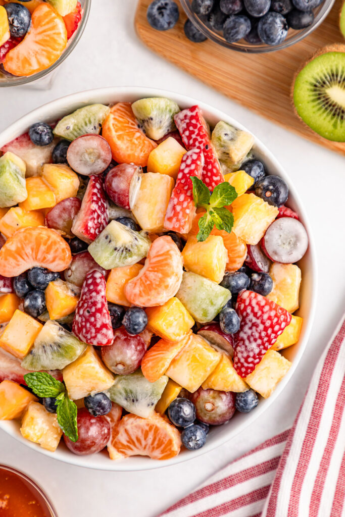 creamy fruit salad in bowl with fruit surrounding it