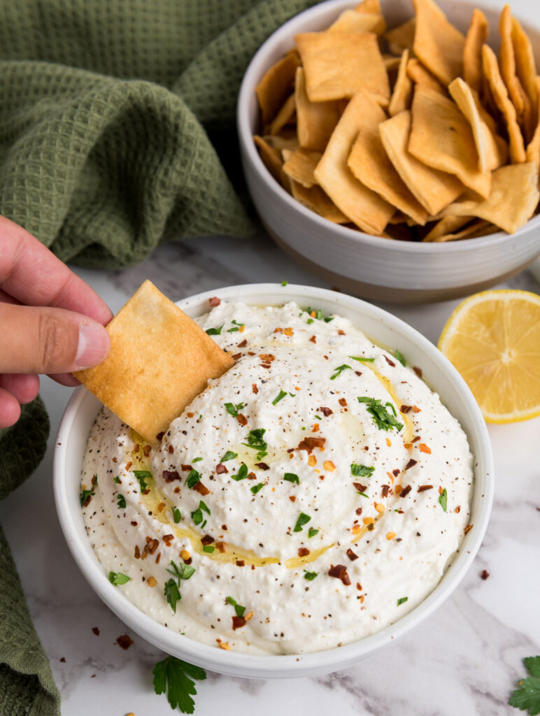 hand dipping square cracker into whipped feta dip