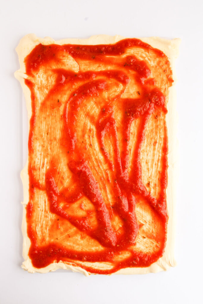 rectangle shaped dough with pizza sauce spread over it