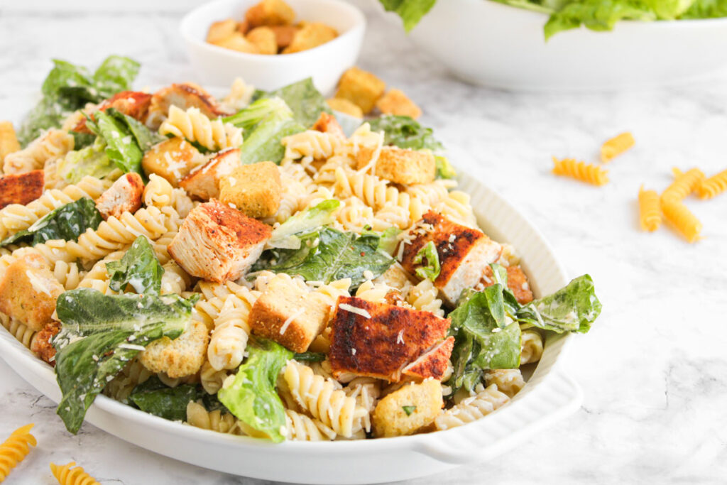 white serving dish with chicken caesar pasta salad