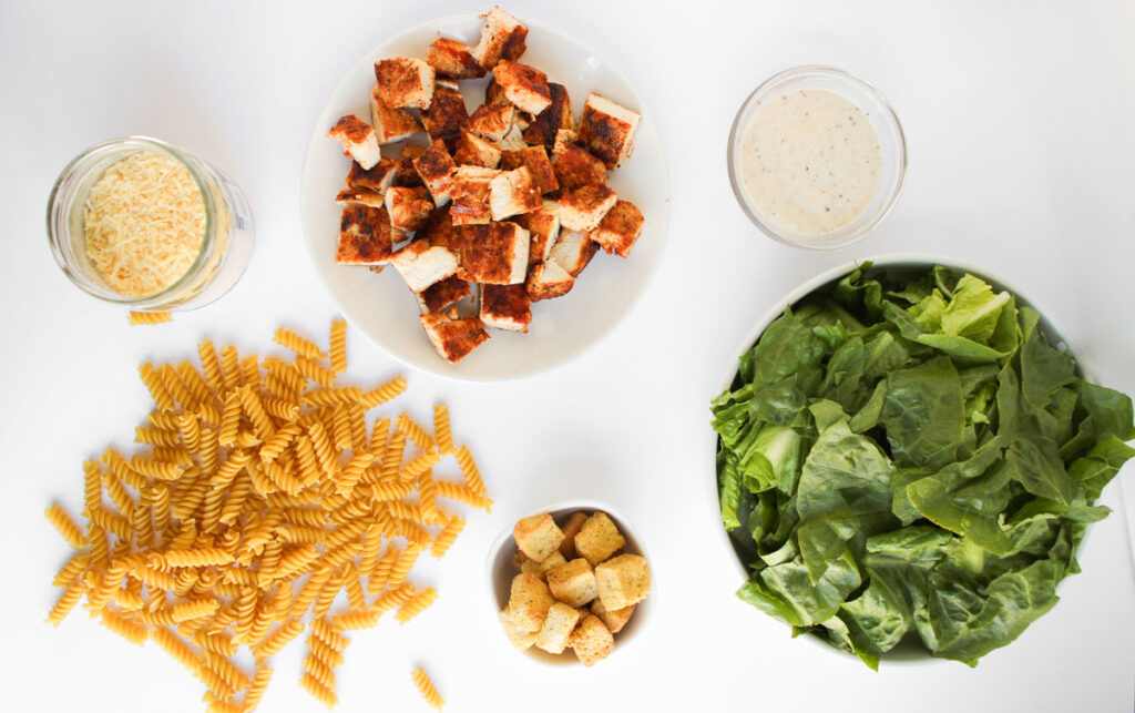chicken caesar pasta salad ingredients in bowls on counter