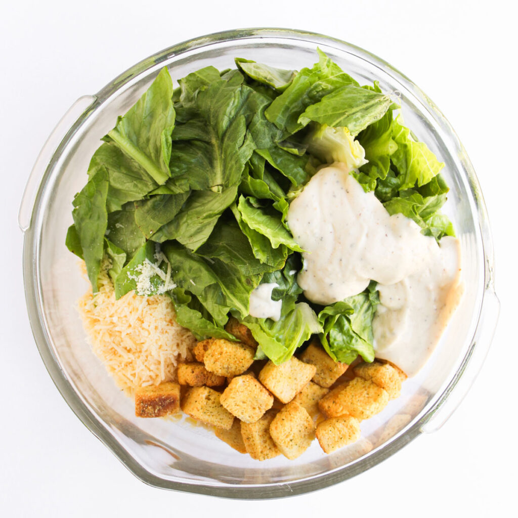chicken caesar pasta salad ingredients in glass bowl