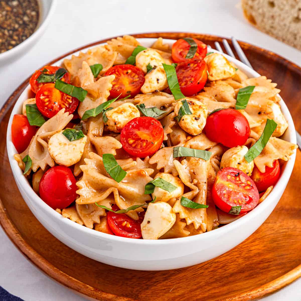 caprese pasta salad in white bowl on wood plate