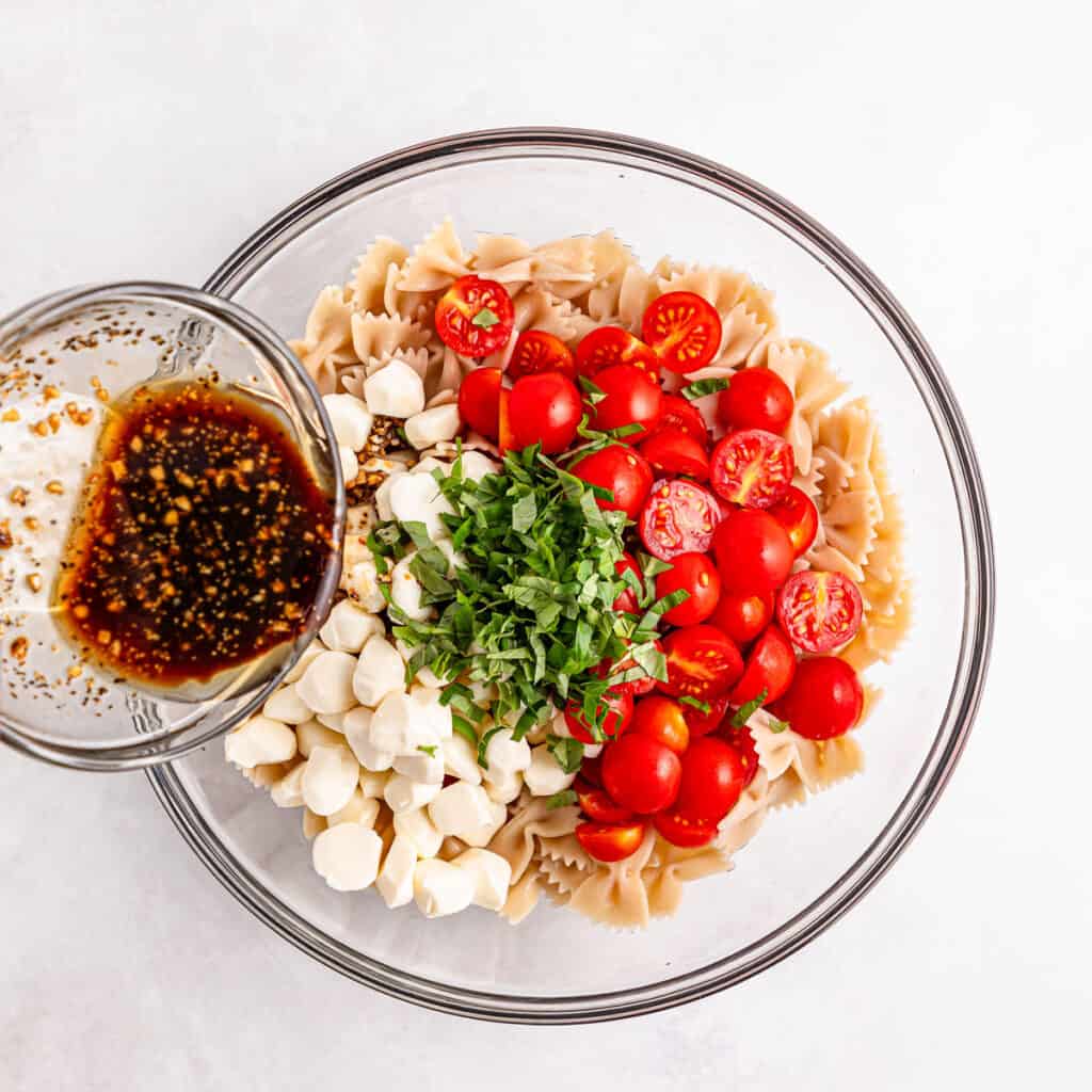 adding dressing to caprese pasta salad