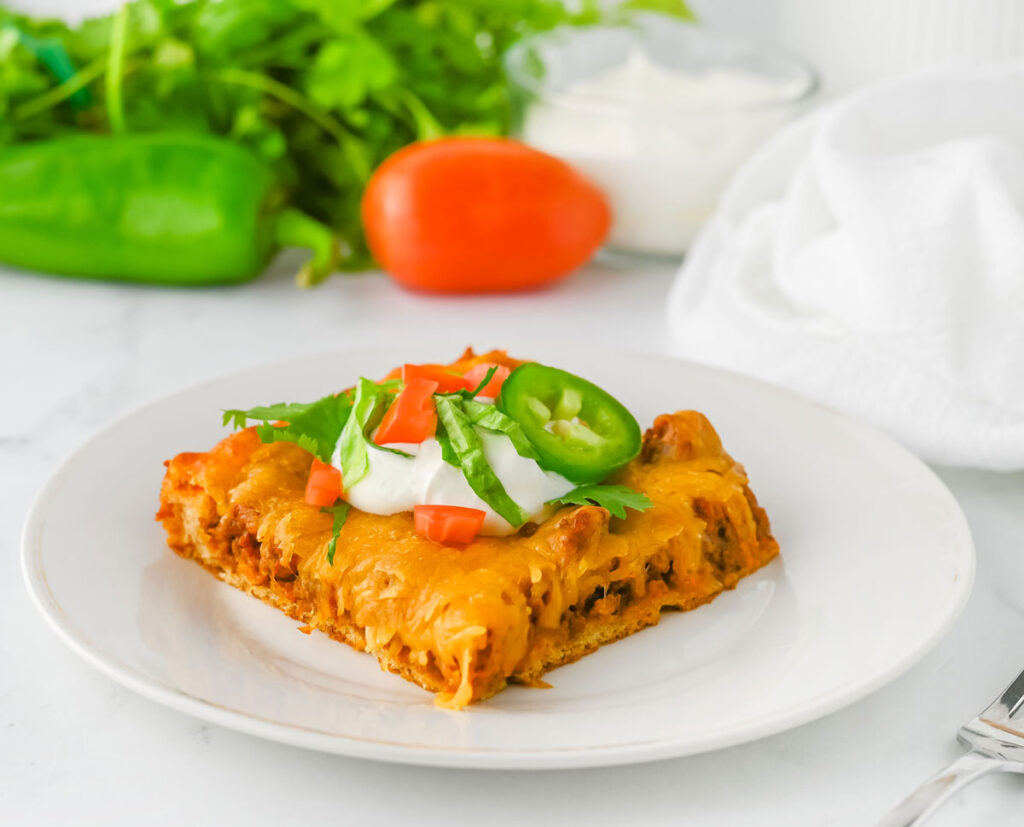 portion of crescent taco bake on white plate topped with sour cream and slice of jalapeno