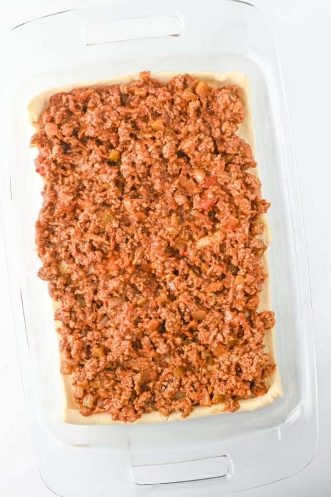 ground beef over crescent roll dough in glass casserole dish