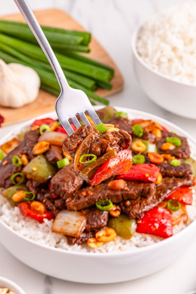 fork in bowl of kung pao beef over rice in white bowl