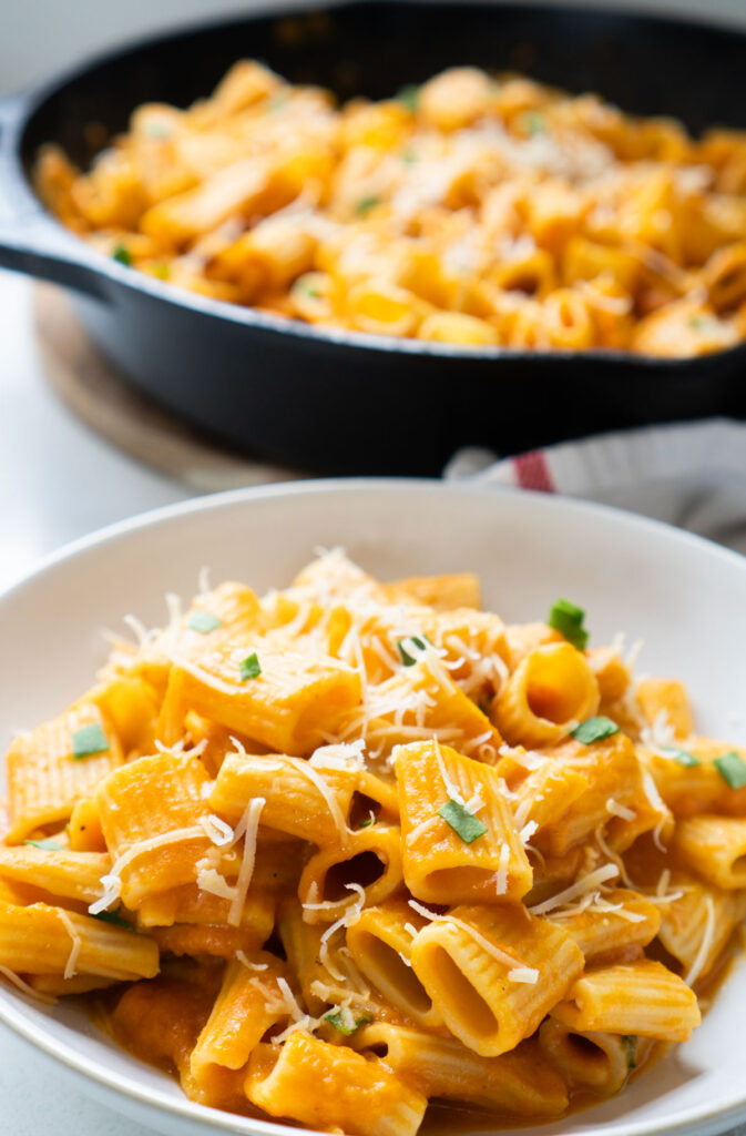 creamy pumpkin pasta in white bowl in frotn of skillet of pasta