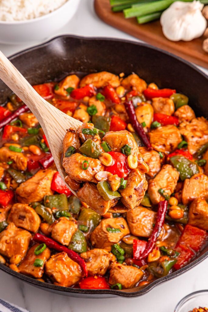 wooden spoon scooping kung pao chicken out of skillet