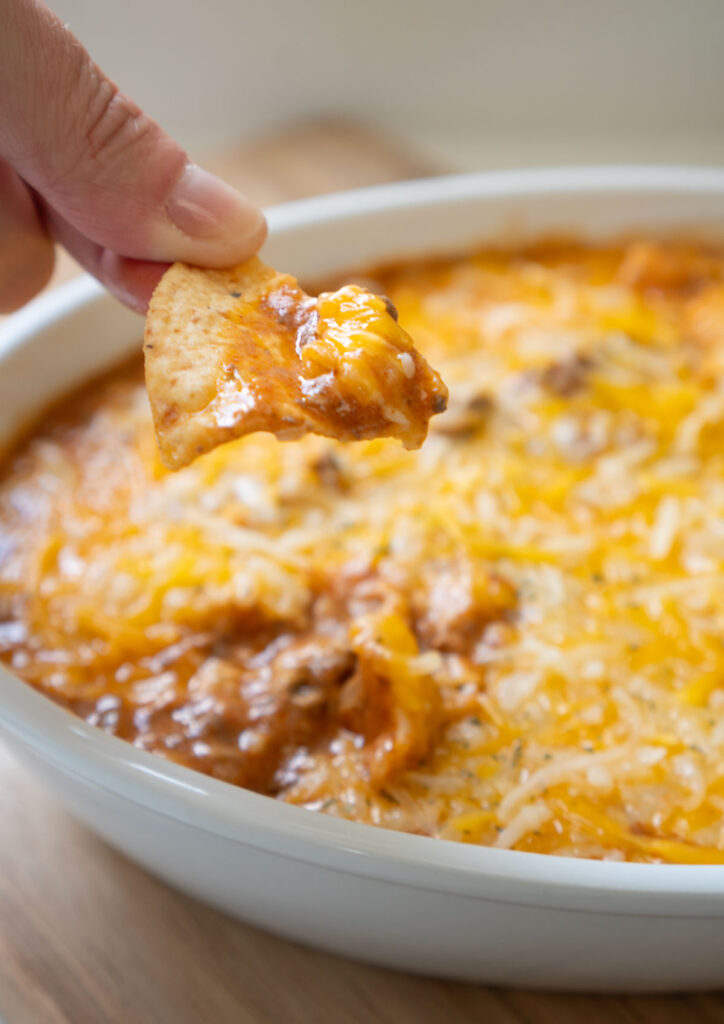 chip scooping up some enchilada dip from serving dish